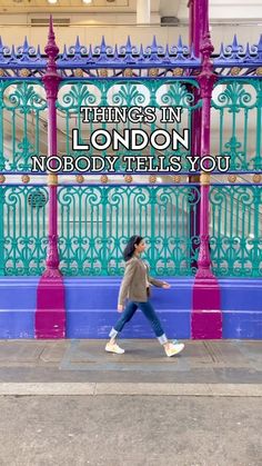 a woman walking down the sidewalk in front of a blue and purple fence with text that reads, things in london nobody tells you