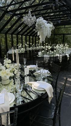 a table set up with white flowers and candles for a formal dinner in a greenhouse