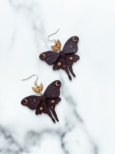 two purple butterflies with gold accents on them are hanging from the back of a pair of earrings