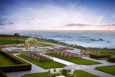 an outdoor wedding setup with chairs and tables on the lawn overlooking the ocean at sunset