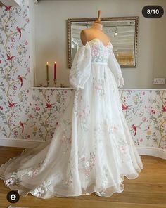 a wedding dress on display in front of a wallpapered room with candles and a mirror