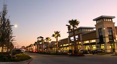 an empty street at dusk with palm trees in the foreground and shops on both sides