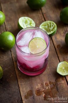 a drink with limes around it on a wooden table