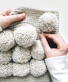 someone is crocheting the pom - poms on a blanket with their hands