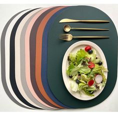 a white plate topped with a salad next to fork and knife on top of a striped place mat