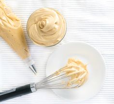 a white plate topped with whipped cream next to a whisk filled with peanut butter