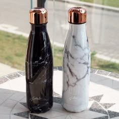 two black and white marble bottles sitting on top of a table next to each other