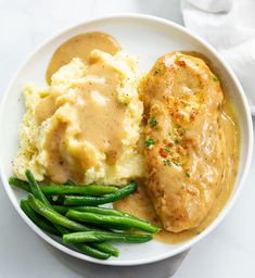 a white plate topped with mashed potatoes and green beans next to gravy