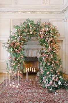 a floral arch with candles and flowers on the floor in front of a fire place