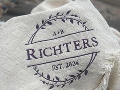 a close up view of the logo on a white cloth with purple letters and leaves