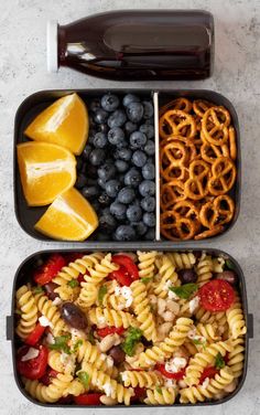 two trays filled with pasta, fruit and pretzels next to a bottle of soda