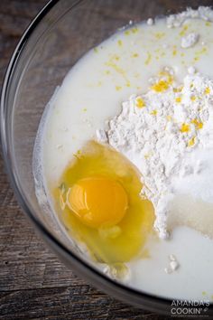 ingredients in a glass bowl on top of a wooden table, including eggs and flour