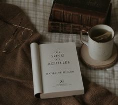 the song of achilles by madeleine millier is next to an old book and glasses