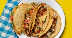 three tacos sitting on top of a white plate next to a blue and white checkered napkin