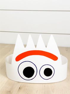 a paper crown with eyes on it sitting on top of a wooden floor next to a white wall