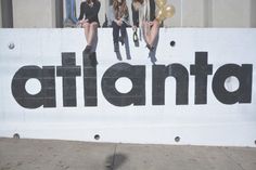 three women sitting on top of a giant sign that says atlanta with balloons in the air