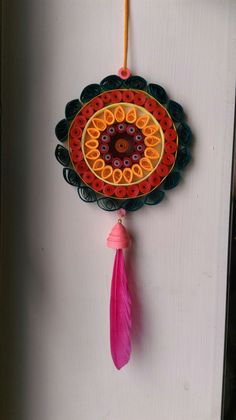 a colorful wall hanging with a pink tassel on the end and an orange piece of paper attached to it