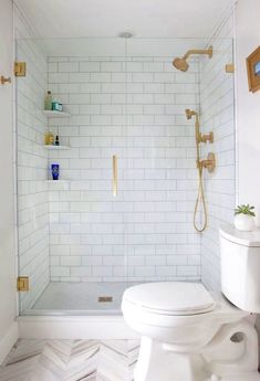 a white toilet sitting in a bathroom next to a walk in shower with gold fixtures