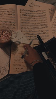 someone is writing notes in front of an open book with music sheets and a bowl of marshmallows