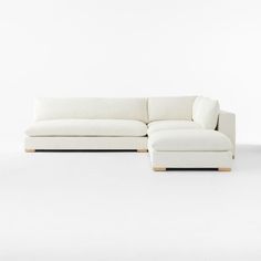 a white couch with a wooden foot rest on the bottom right side and an ottoman in the middle