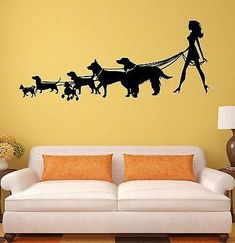 a living room with a couch and a wall decal that has a woman walking two dogs on a leash