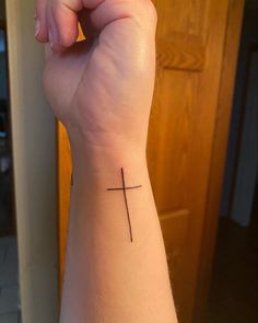 a person's wrist with a small cross tattoo on the middle of their arm