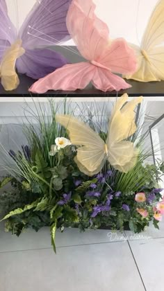 three different colored butterflies sitting on top of a planter filled with flowers and greenery