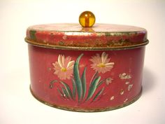 an old tin box with flowers painted on the side and a yellow object in the middle