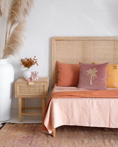 a bed with pink and orange pillows on top of it next to a white vase