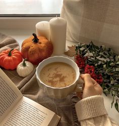 a person is holding a cup of coffee in front of an open book and pumpkins