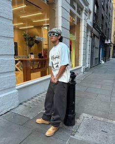 a man is standing on the sidewalk in front of a store wearing sunglasses and a t - shirt