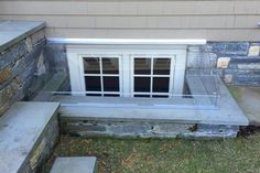 a window sitting on the side of a stone wall next to steps and grass in front of it