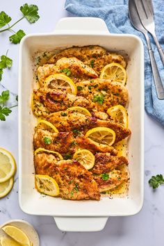 a casserole dish with chicken, lemons and parsley on the side