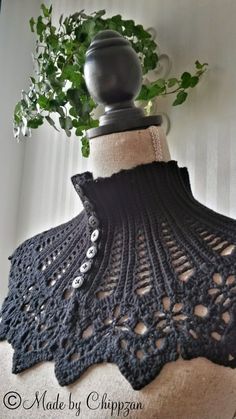 a black crocheted shawl with buttons on it and a plant in the background