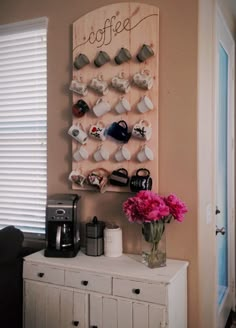 a coffee bar with pink flowers in a vase next to a wall mounted cup holder