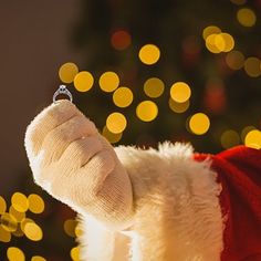 a santa claus hat with a ring hanging from it's middle finger in front of a christmas tree