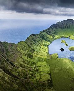 an aerial view of some green hills and lakes in the middle of it with dark clouds overhead