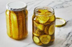 two jars filled with pickles sitting on top of a marble counter next to each other