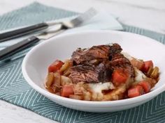 a bowl filled with meat and vegetables on top of a blue table cloth next to utensils