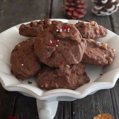 chocolate cookies with sprinkles in a white bowl on a wooden table next to pine cones