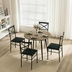 a dining room table with four chairs and a vase on top of it in front of a window