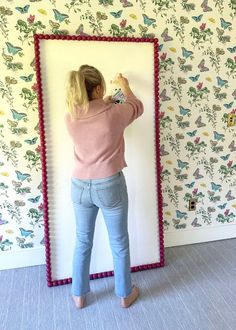 a woman standing in front of a wall with butterflies on it and holding a paintbrush