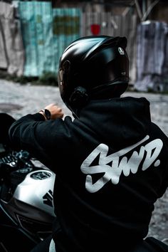 a man riding on the back of a motorcycle wearing a black shirt with white writing