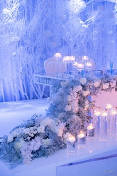 a table topped with lots of white flowers and candles next to a wall covered in snow