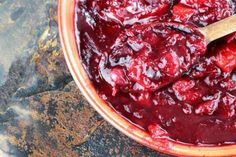 a bowl filled with cranberry sauce on top of a stone counter next to a wooden spoon