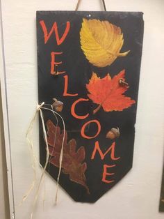 a welcome sign hanging from the side of a door with autumn leaves on it,