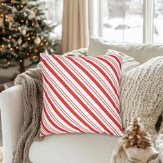 a red and white pillow sitting on top of a couch next to a christmas tree