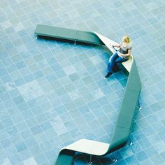 a woman sitting on a bench in the middle of a tiled floor with an arrow shaped bench next to her