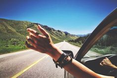 a person is driving down the road with their hand up in the air and mountains behind them