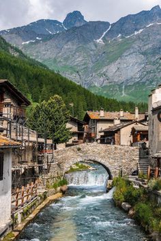 a river running through a small town with mountains in the background